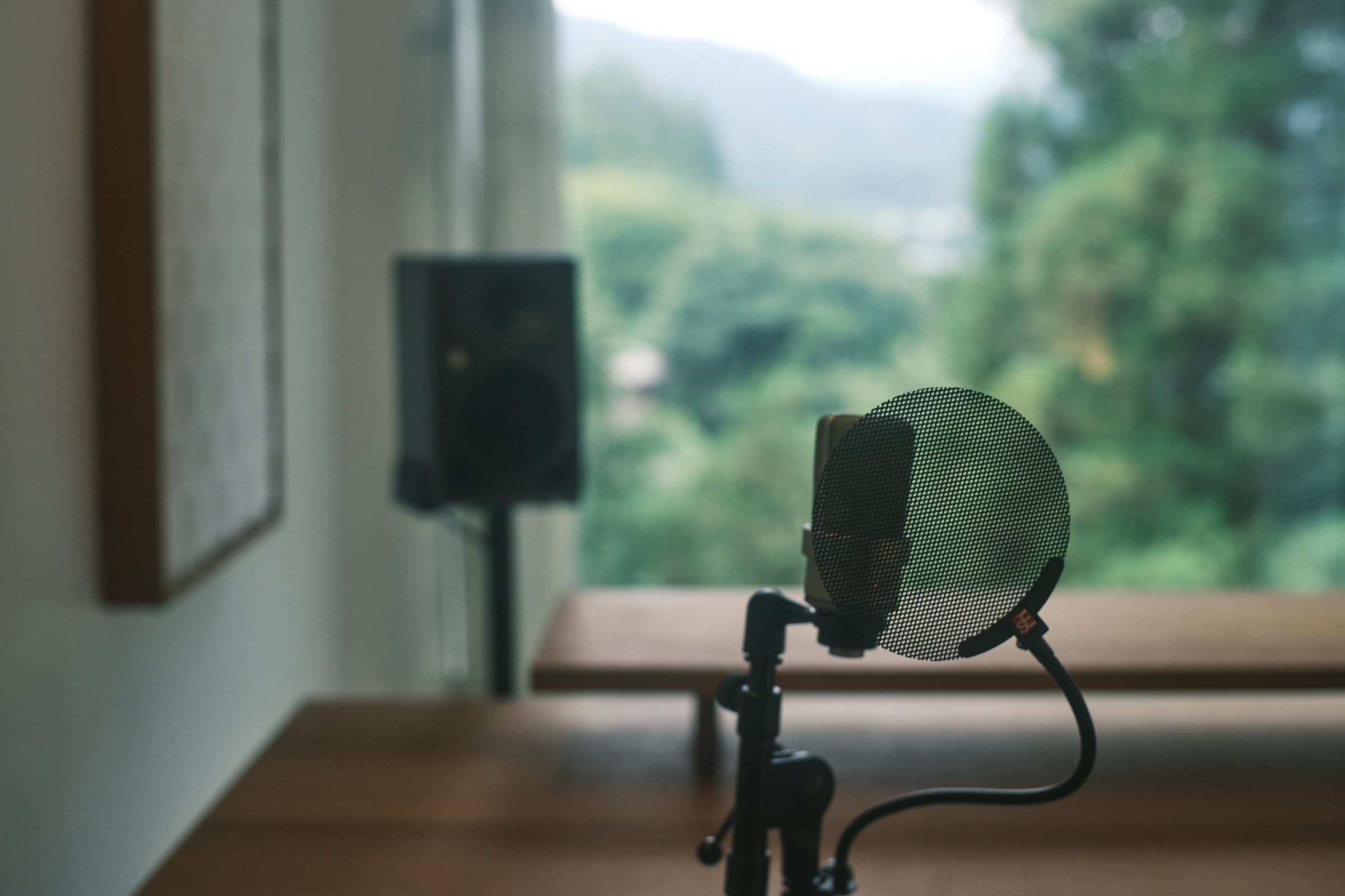 Microphone with a pop filter facing the window, monitor speaker and mountain view in the background